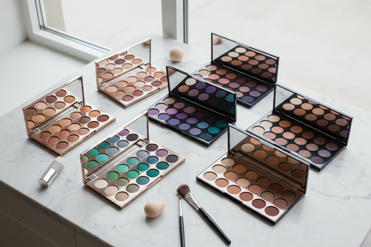 Collection of eyeshadow palettes in bronze, purple, green, and neutral tones arranged on white marble surface - eyeshadow color guide for different eye colors